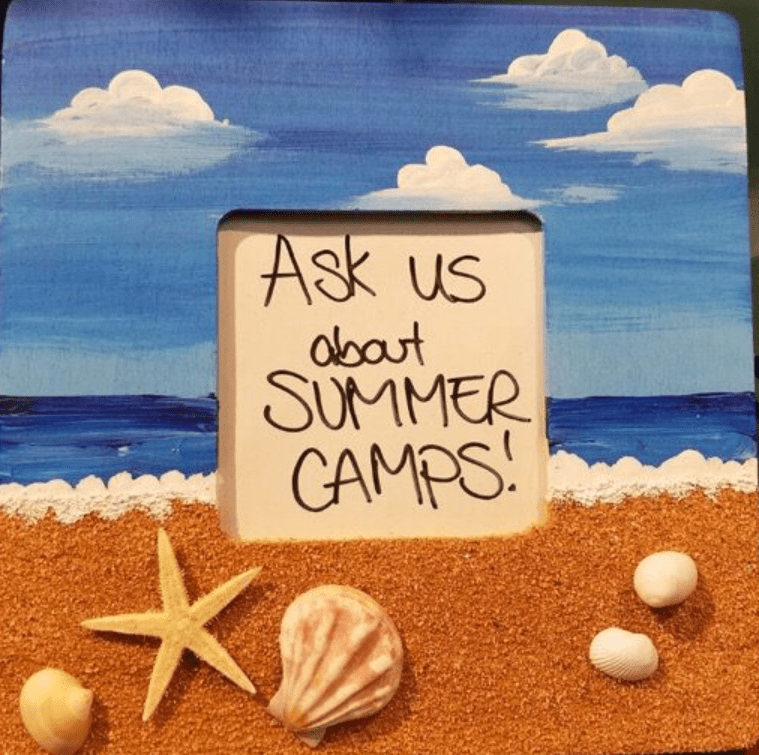 a frame with a sign and seashells on the beach.